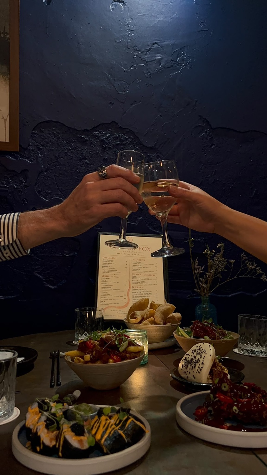 A shared table of Japanese-inspired food and raised glasses